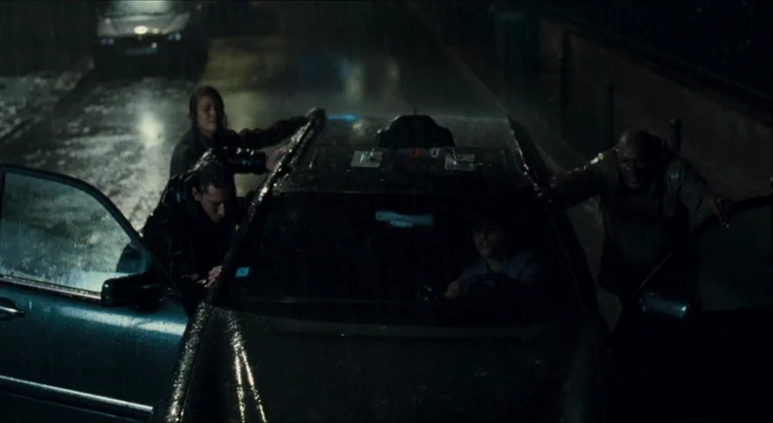 35 Shots of Rum (2008) movie still: wide — A dark, rain-slicked city street at night features a sedan stopped on the road. Three people surround the…