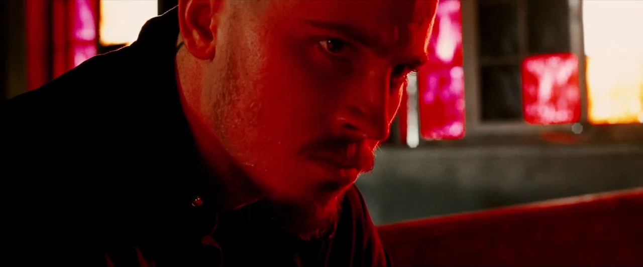Death Sentence (2007) movie still: closeup — A dark room features red stained glass windows casting bright crimson light. A man with a goatee looks…