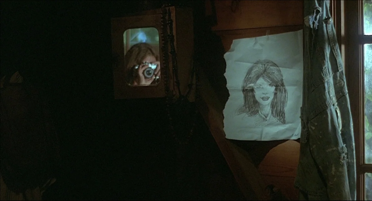 The Howling (1981) movie still: medium — A dimly lit room features a charcoal sketch pinned to wooden wall paneling. A woman's reflection appears in…