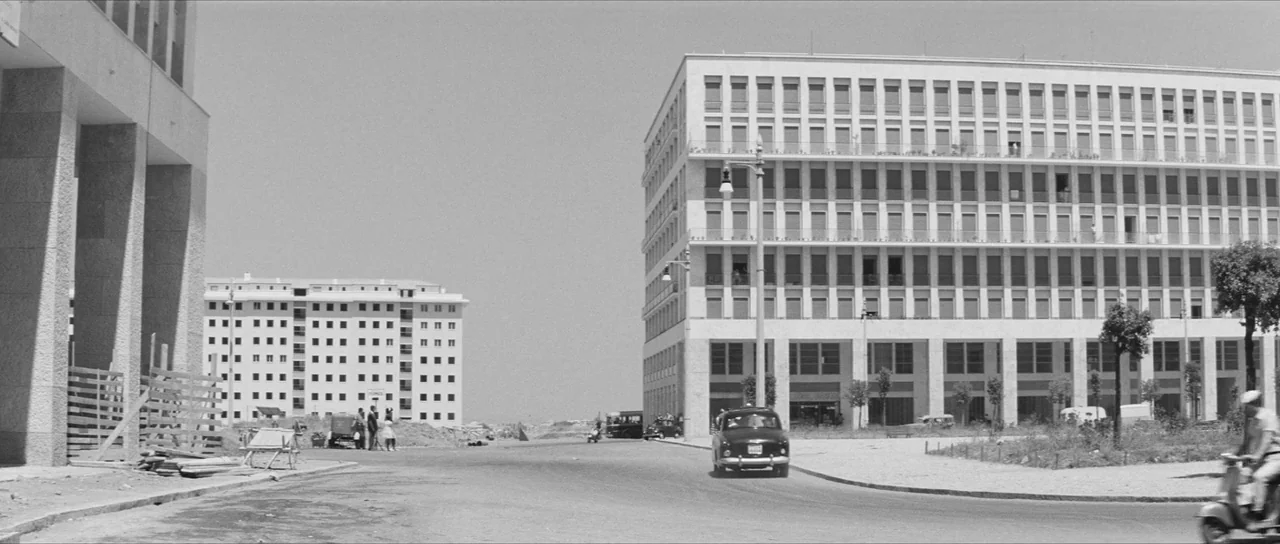La Dolce Vita (1960) movie still: establishing — Wide outdoor shot of a sparse, modern urban landscape with large concrete apartment blocks. A…