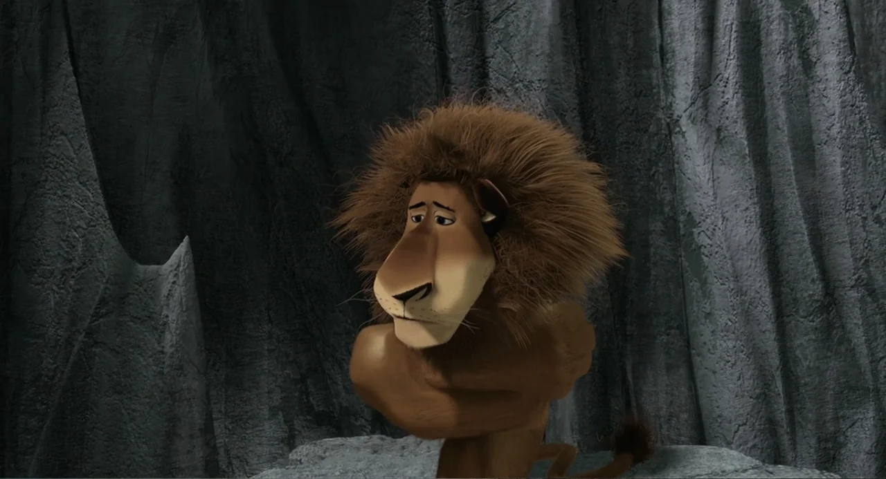 Madagascar (2005) movie still: medium — A dark rocky cave interior with textured grey stone walls. A lone anthropomorphic lion stands with his arms…