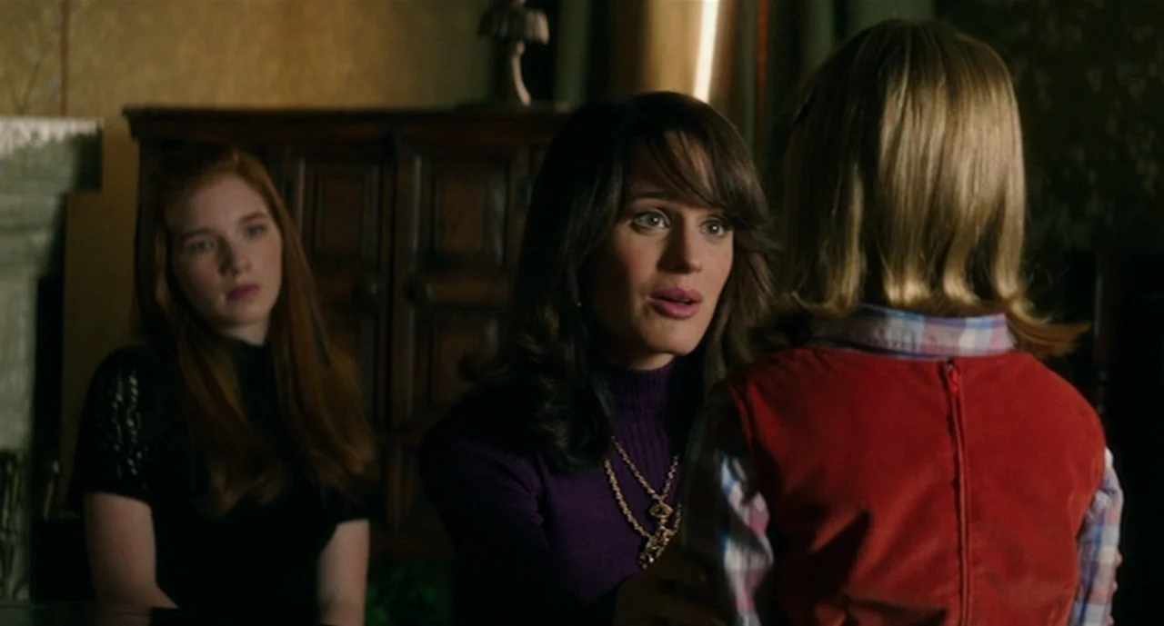 Ouija: Origin of Evil (2016) movie still: medium — A dimly lit room with vintage decor features a woman and two young people. The woman speaks to a…