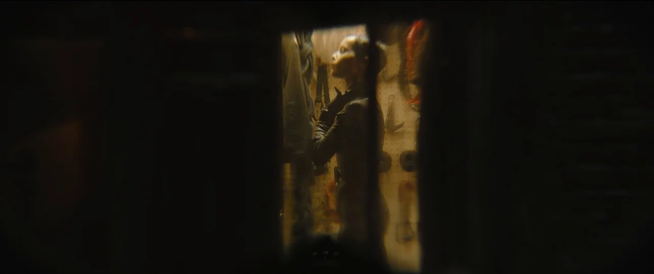 The Batman (2022) movie still: medium — A dark workshop space features a tool-covered pegboard wall visible through a narrow frame. A woman stands…