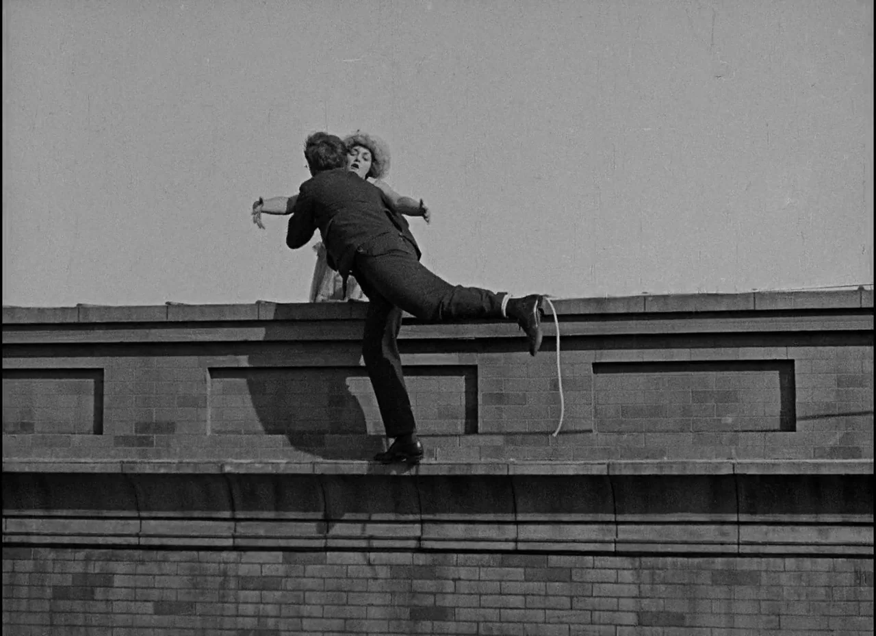 Safety Last! (1923) movie still: fullbody — Two individuals interact on the narrow ledge of a structured brick wall. The man supports the woman as…