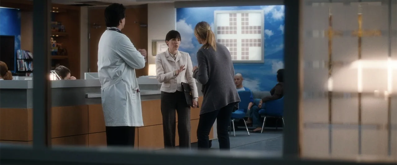 My Sister's Keeper (2023) movie still: medium — A modern hospital waiting area features a reception desk and a wall mural. Two women and a doctor in…