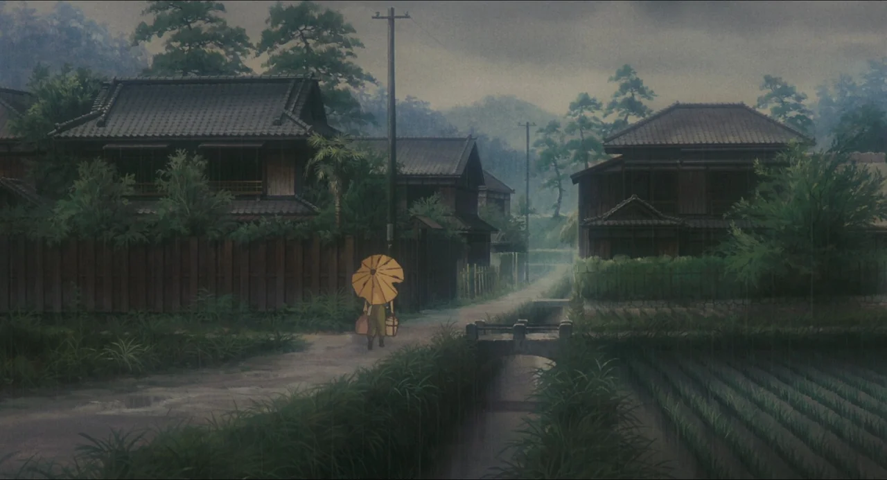 Grave of the Fireflies (1988) movie still: wide — A rural village path runs between wooden houses and rice paddies in the rain. A lone figure…