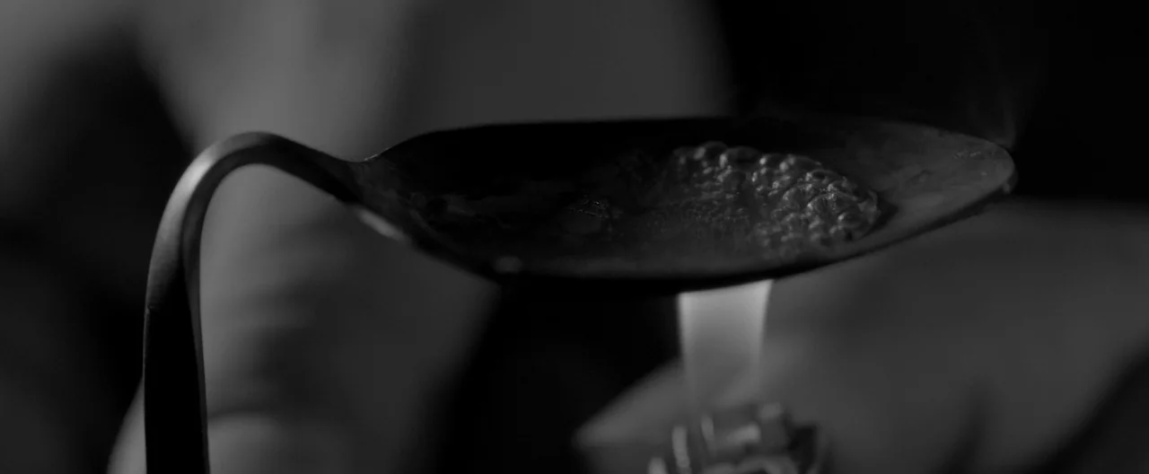 A Girl Walks Home Alone at Night (2014) movie still: closeup — A metal spoon containing a boiling liquid is positioned directly above a small flame.…