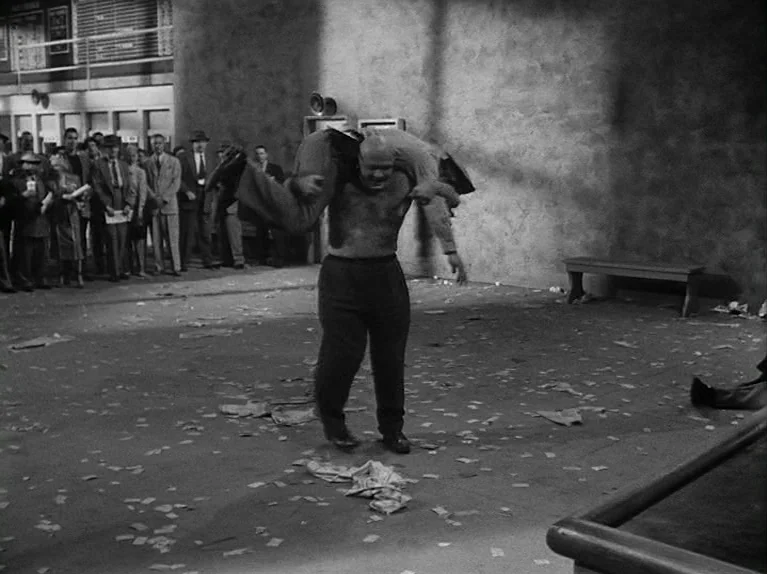 The Killing (1956) movie still: fullbody — A spacious, littered locker room floor features a crowd of spectators in the background. A large…
