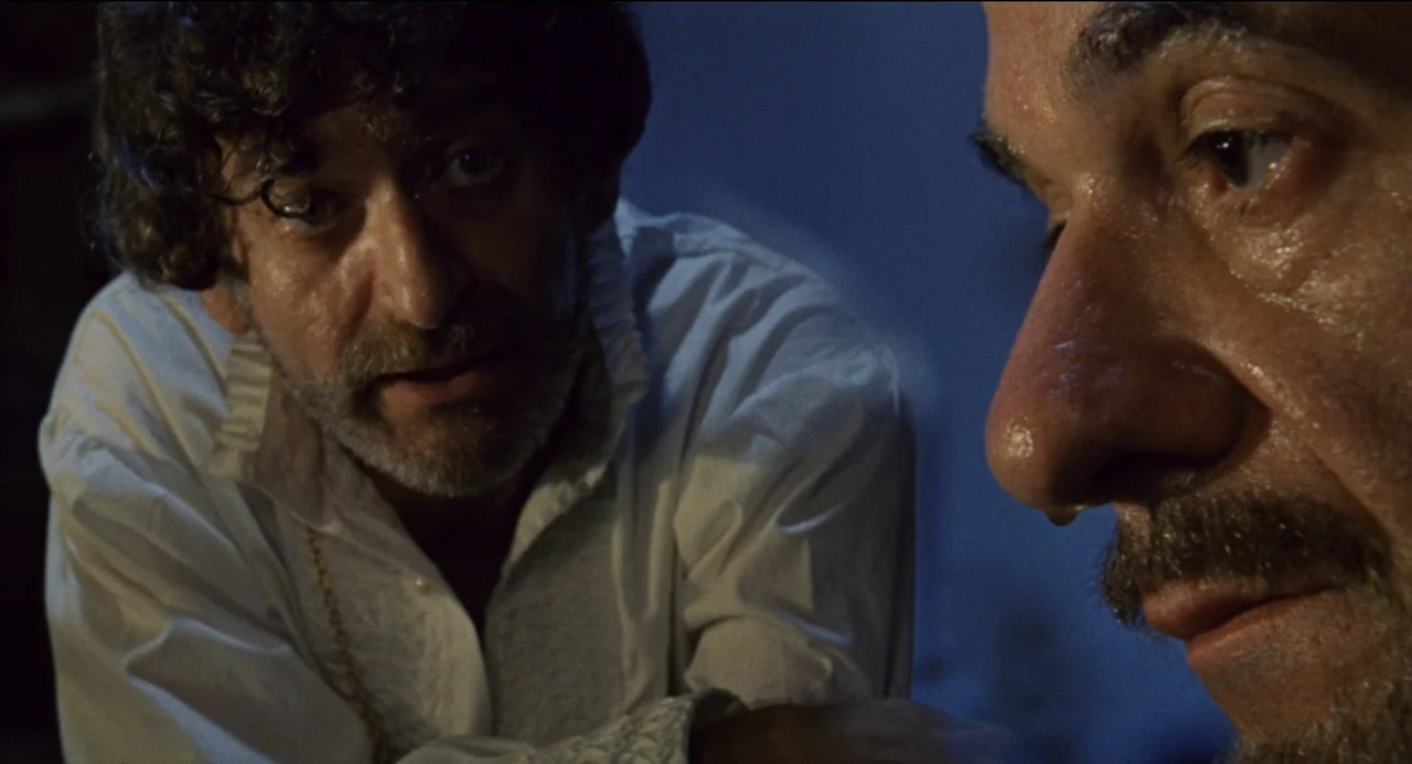 Beatrice Cenci (1969) movie still: medium — A dark indoor space with cool tones and minimal visible features in the background. Two men face each…