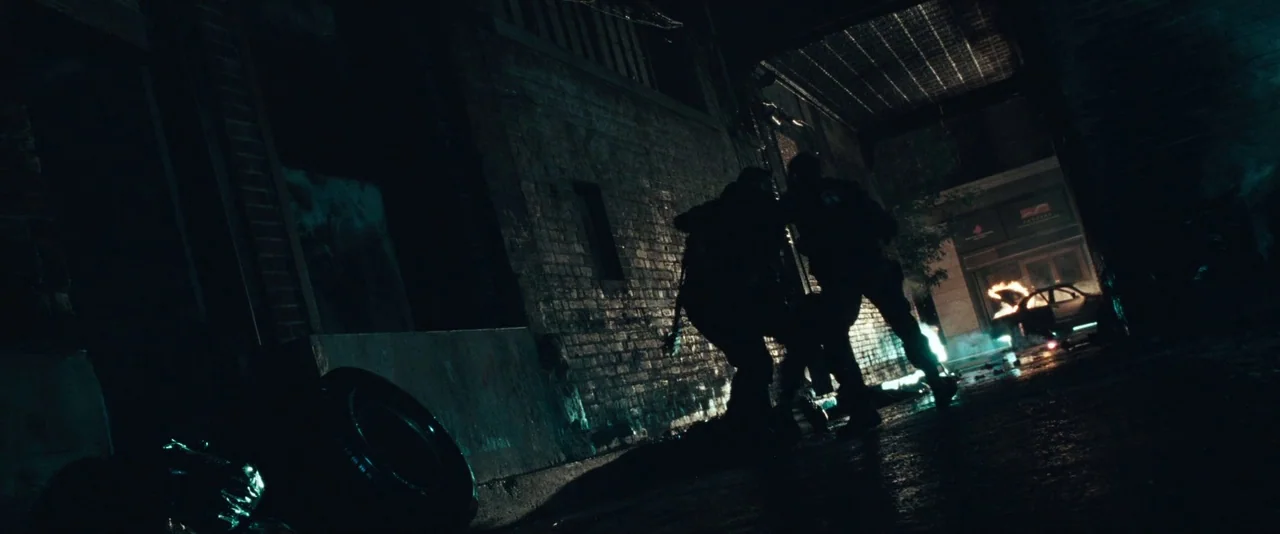 Resident Evil: Apocalypse (2004) movie still: wide — A dark brick alleyway at night holds two silhouettes walking toward a distant fire. A burning…