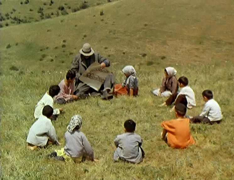 The Wishing Tree (1977) movie still: wide — A grassy hillside with gentle slopes is covered in sparse, yellowish-green wild meadow grass. A man sits…