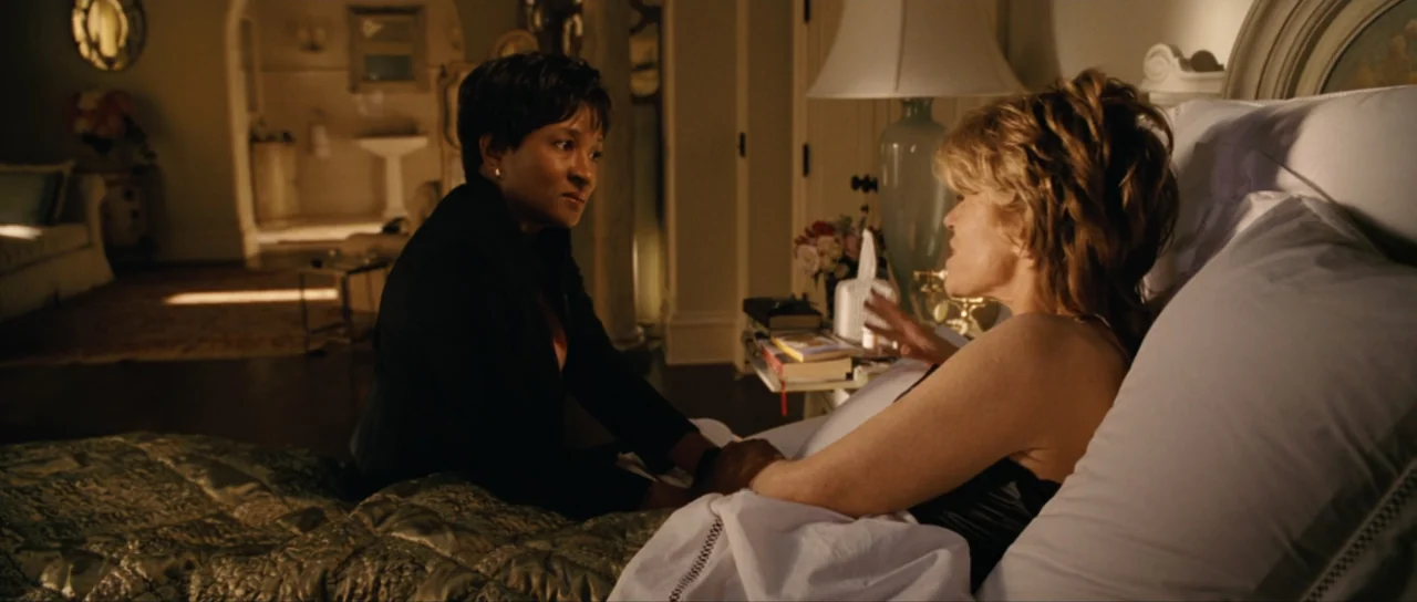 Monster-in-Law (2005) movie still: medium — A well-lit bedroom features a plush bed with quilted bedding and a lamp. Two women sit facing each other…