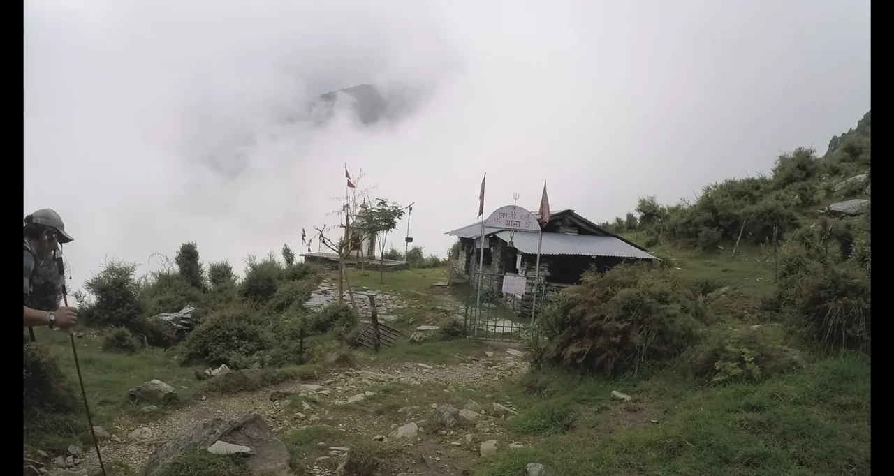 Blutch (2018) movie still: wide — A stone building with a metal roof stands on a foggy alpine ridge path. Sparse vegetation and rocky terrain…