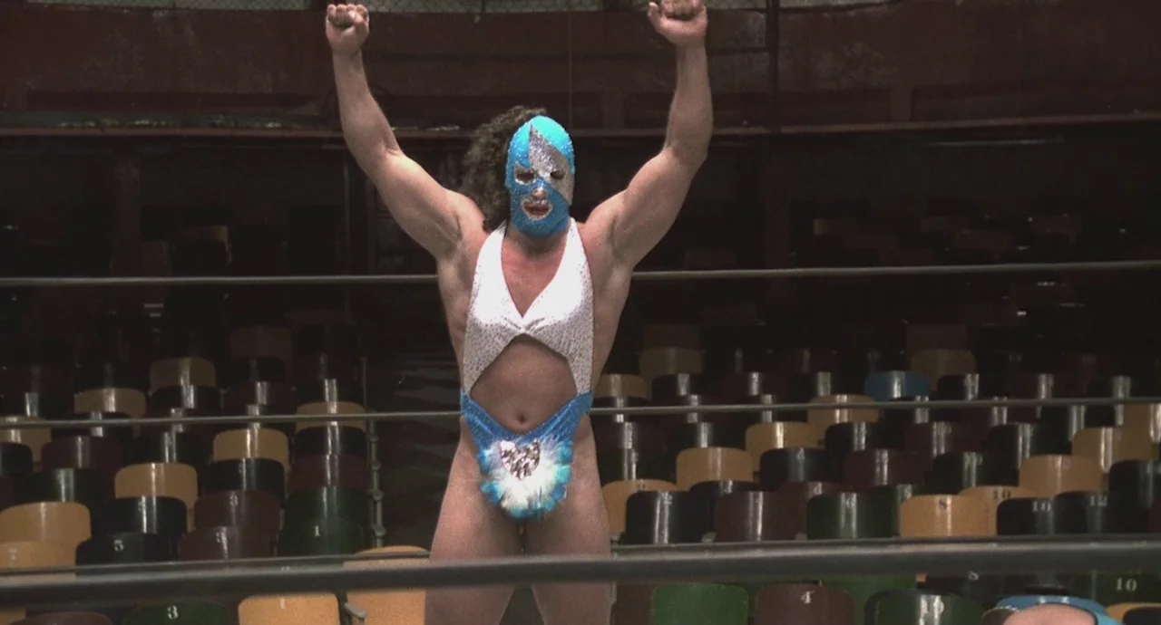 Santa Sangre (1989) movie still: fullbody — A wrestling arena features rows of numbered empty chairs facing the central ring. A wrestler wearing a…