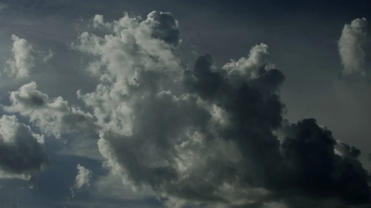 The Dalton Gang (2020) movie still: establishing — A dense formation of cumulus clouds floats through a grey daylight atmosphere. Light reflects off…