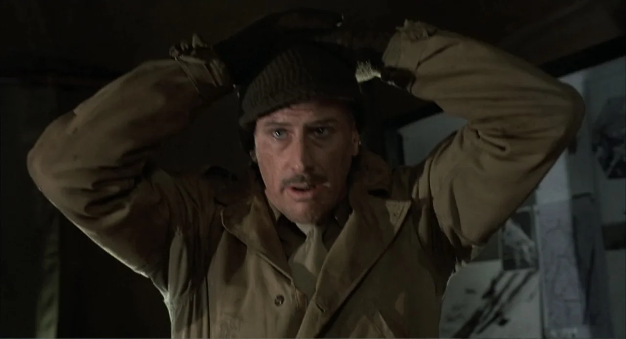 Zone Troopers (1985) movie still: medium — A dimly lit interior space with canvas walls suggesting a military field tent. A man wears a tan trench…