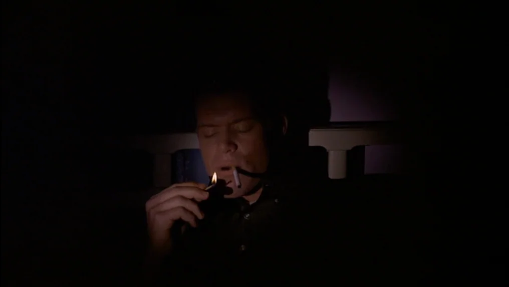 Targets (1968) movie still: closeup — A dark, dimly visible bedroom space serves as the setting for the shot. A man lights a cigarette with a small…