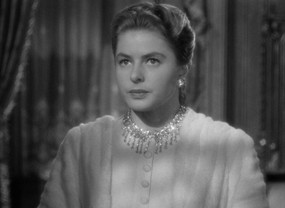 Notorious (1946) movie still: medium — A well-lit interior setting featuring ornate wood-paneled walls and classic decorative curtains. A woman in a…