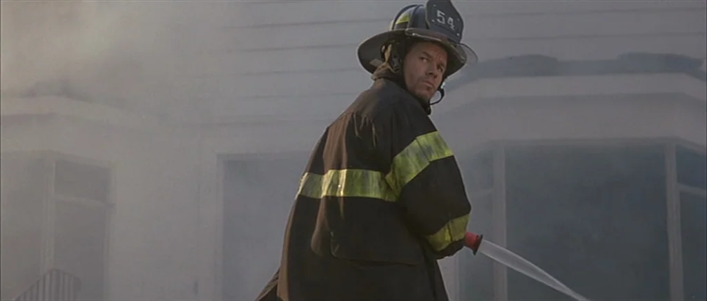 I Heart Huckabees (2004) movie still: medium — A firefighter in protective gear operates a hose in front of a smoke-filled house. The subject stands…