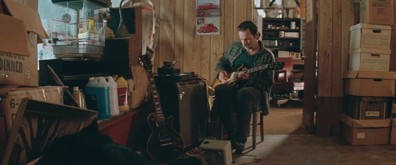 The Sweet Hereafter (1997) movie still: medium — A cluttered room features wood paneled walls, numerous cardboard boxes, and various musical…