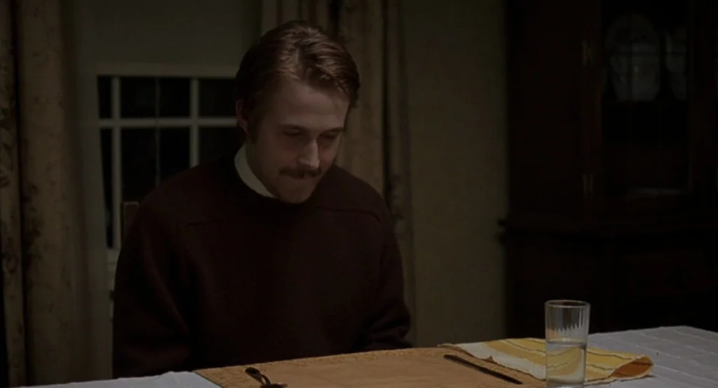 Lars And The Real Girl (2007) movie still: medium — A dimly lit room with brown drapes and an empty placemat set on the table. A man in a brown…