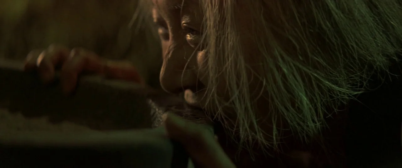 Ballad Of Narayama (1958) movie still: closeup — An aged woman rests her chin on the edge of a dark stone ledge. Her face is partially obscured by…