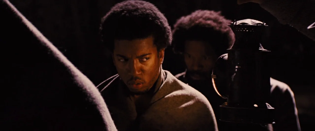 Django Unchained (2012) movie still: medium — Two men stand in a dense, dark forest during the nighttime. One man holds a metal lantern,…