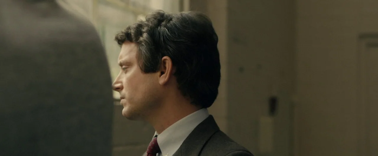 No Man of God (2021) movie still: medium — An interior space with beige walls and a window providing natural daylight. A man in a business suit…