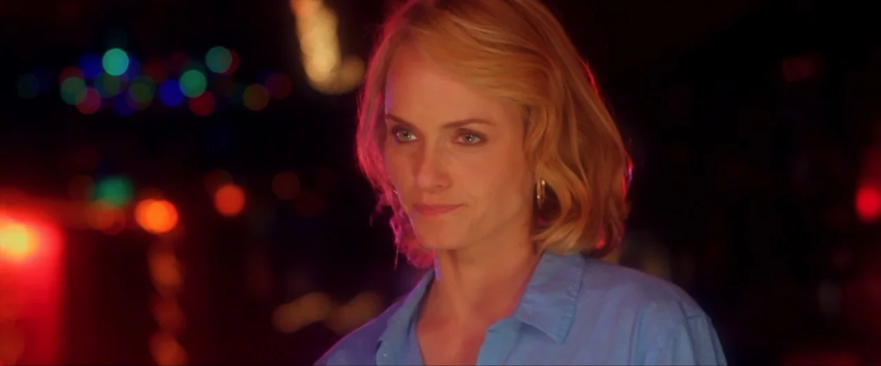 Girl Walks Into a Bar (2011) movie still: closeup — A woman stands in a dimly lit, dark space with blurry colored bokeh lights. She looks toward the…