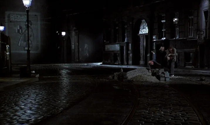 The Serpent’s Egg (1977) movie still: wide — An empty nighttime European street features cobblestones, tram tracks, and a large wall advertisement.…