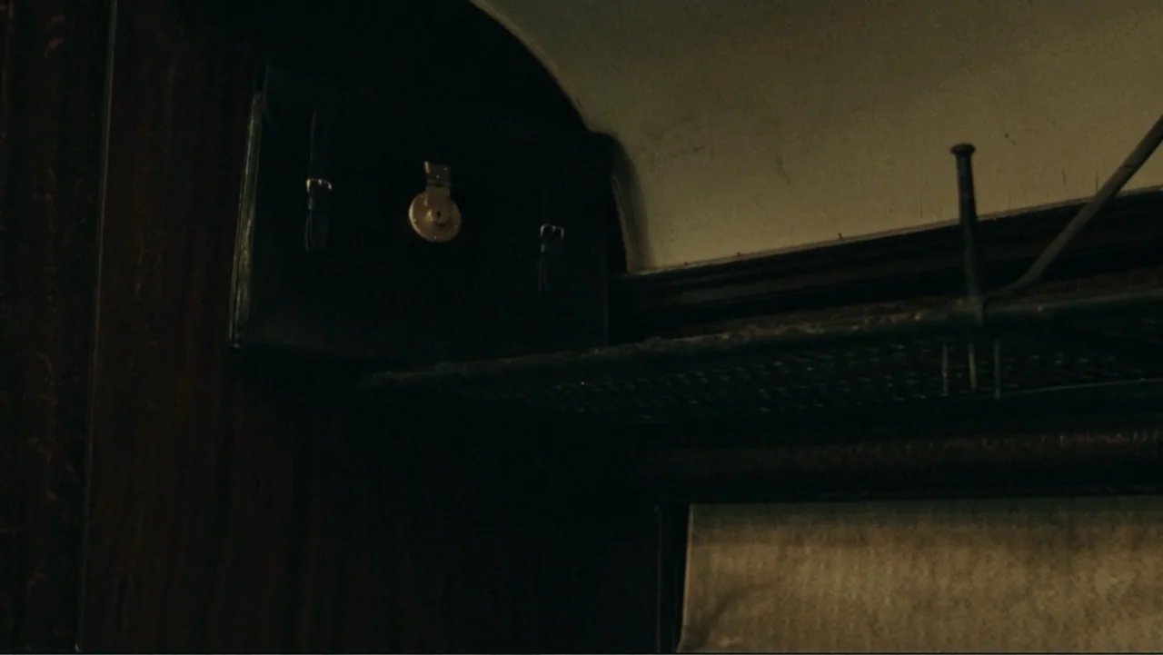 The Words (2012) movie still: closeup — A dark, cramped train interior features a vintage black leather briefcase on a shelf. The luggage rests…