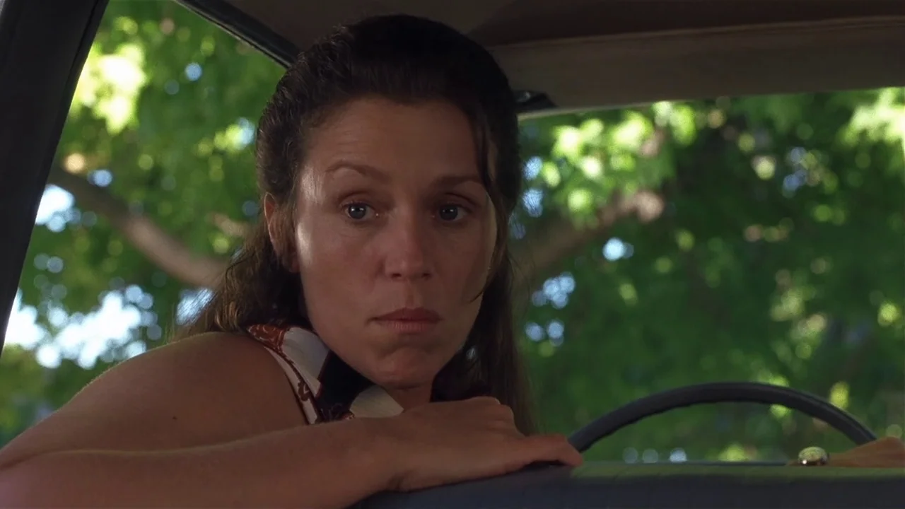 Almost Famous (2000) movie still: closeup — The interior of a car features a steering wheel and a view of trees. A woman leans over the steering…