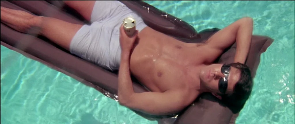 The Graduate (1967) movie still: medium — A man floats on a brown plastic air mattress in a turquoise swimming pool. He holds a metallic beverage…