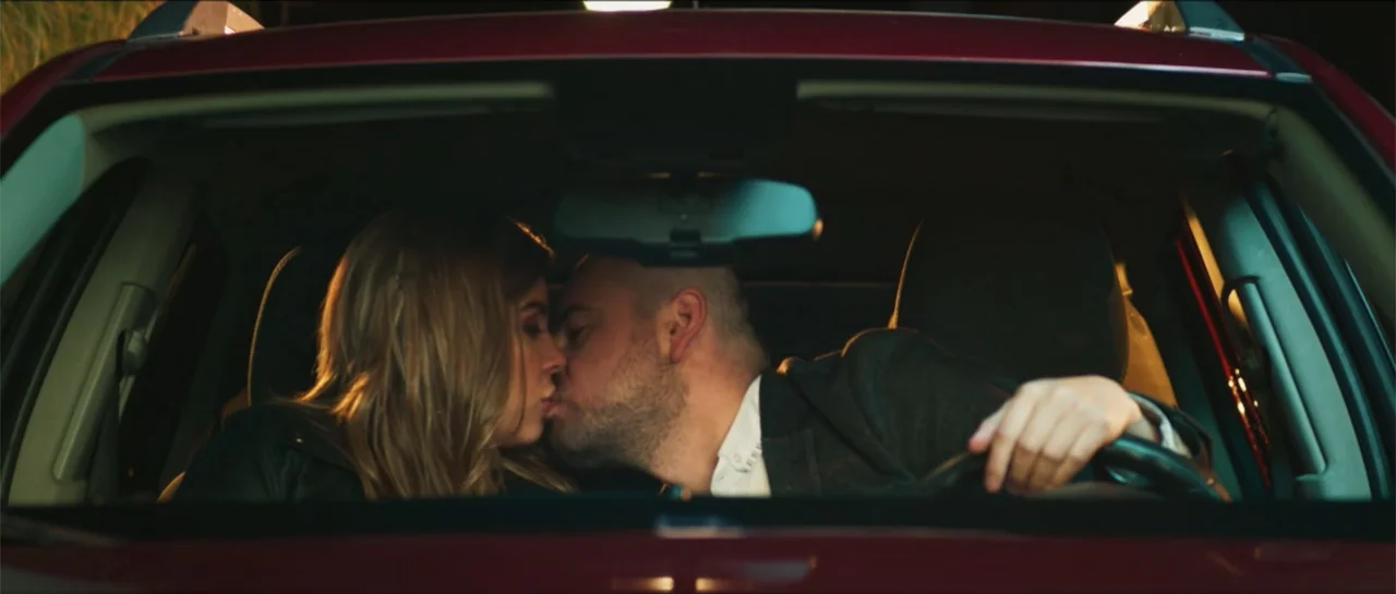 Loving is Losing (2019) movie still: medium — A dark car interior at night with a red exterior frame visible. A man and a woman are positioned in…