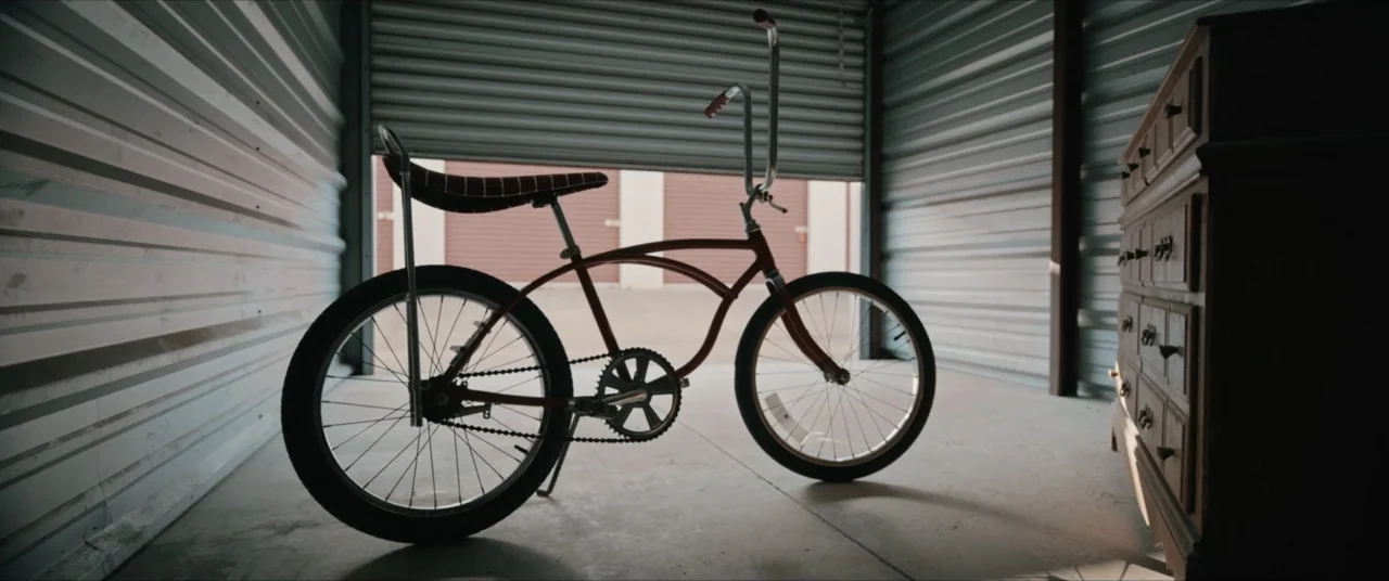 Possessions (2024) movie still: medium — A metal storage unit contains a bicycle and a wooden dresser. The bicycle sits in the center with its front…
