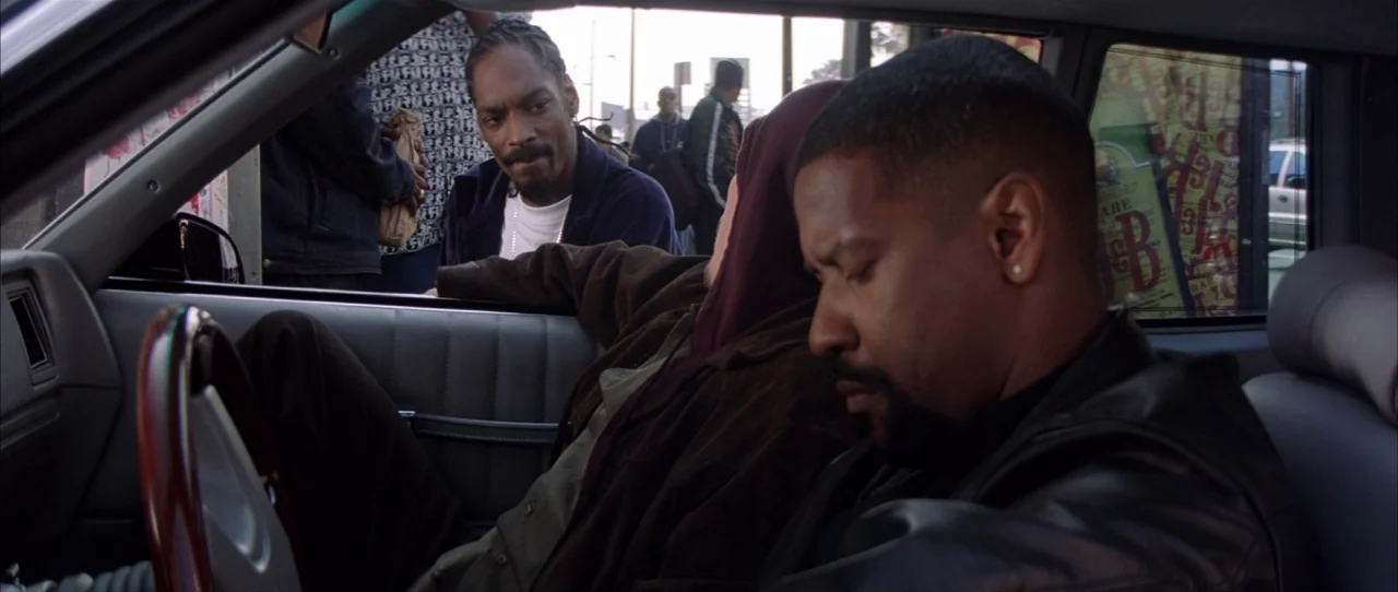 Training Day (2001) movie still: medium — Inside a modern sedan, a man looks down while another man talks through the window. The exterior shows a…