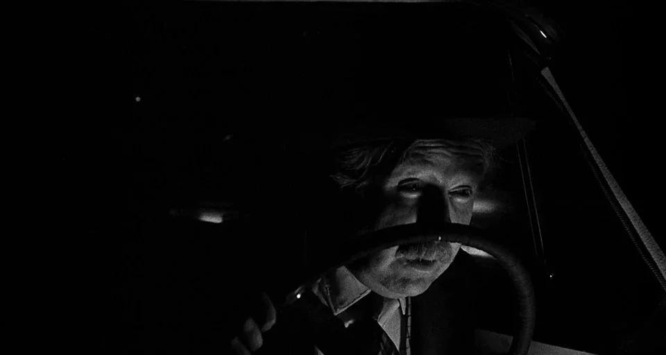 Anatomy of a Murder (1959) movie still: closeup — The interior of a vintage car at night is mostly obscured by deep shadows. A middle-aged man with…