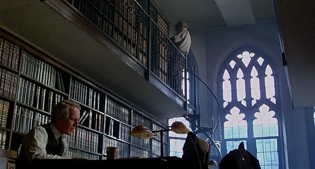 The Verdict (1982) movie still: wide — A high-ceilinged room with floor-to-ceiling shelves packed with books and a spiral staircase. An elderly man…