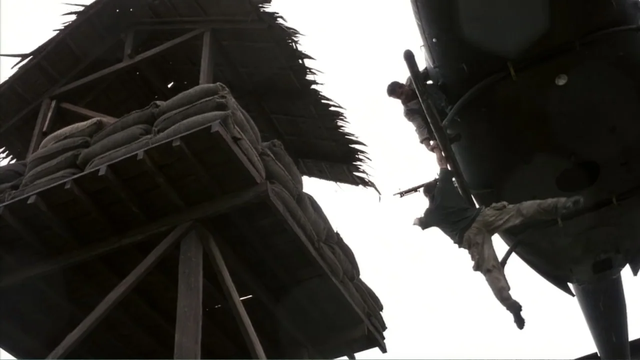 Behind Enemy Lines (2001) movie still: wide — A wooden observation tower stands next to a military helicopter in mid-air. One man clings to the…