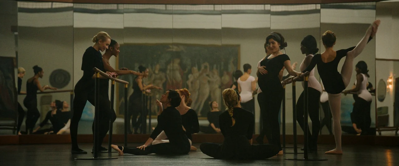 Don’t Worry Darling (2022) movie still: wide — A spacious dance studio features a floor-to-ceiling mirror and a large wall painting. Several dancers…