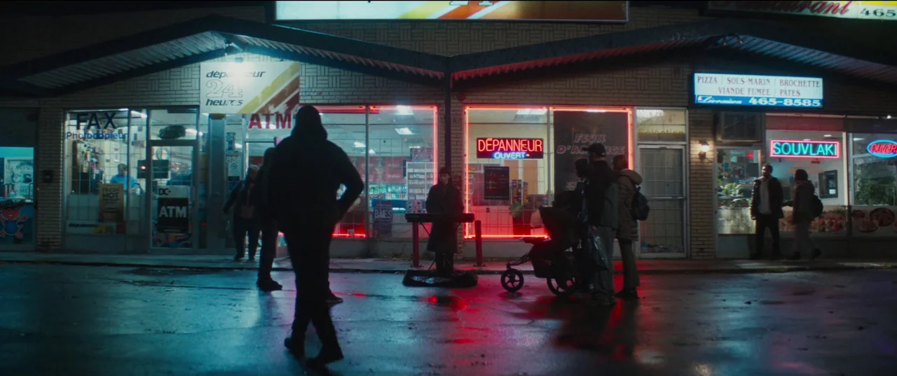 Humanist Vampire Seeking Consenting Suicidal Person (2023) movie still: wide — A nighttime strip mall exterior features illuminated storefront…
