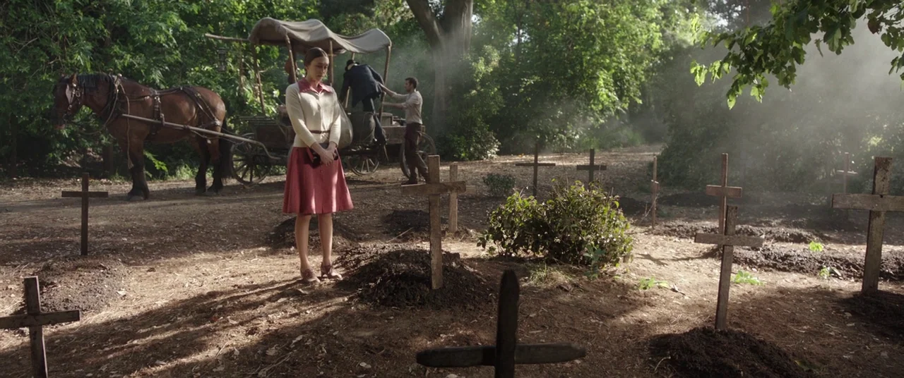 The Nun (2018) movie still: wide — A clearing in a woodland area serves as a rustic cemetery with wooden crosses. A woman stands by a grave while…
