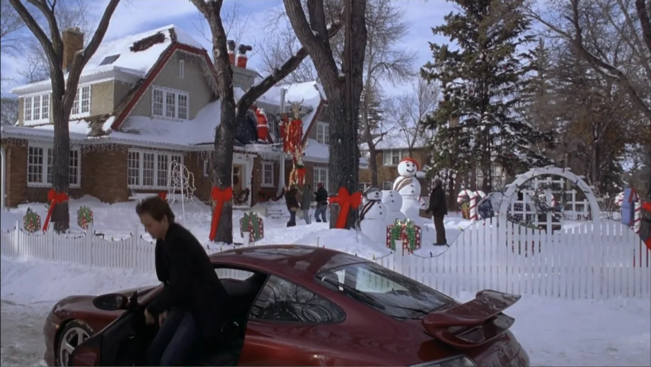 Just Friends (2005) movie still: medium — A snow-covered front yard of a suburban house decorated with Christmas ornaments and snowmen. A man in a…
