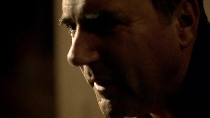 Love Liza (2002) movie still: closeup — A dimly lit indoor space with heavy shadows obscuring most of the environment. A middle-aged man stands in…