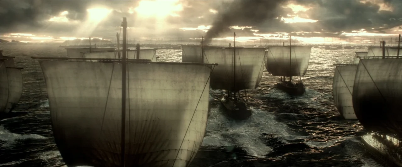 300: Rise of an Empire (2014) movie still: wide — A fleet of ancient wooden ships with square sails navigates a choppy, dark sea. The ships move…