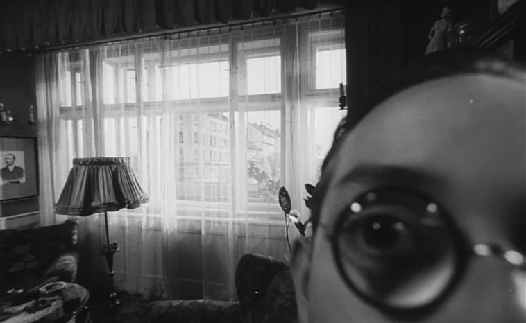 The Cremator (1969) movie still: closeup — An interior space features a large window with white curtains overlooking a city street. A person's right…