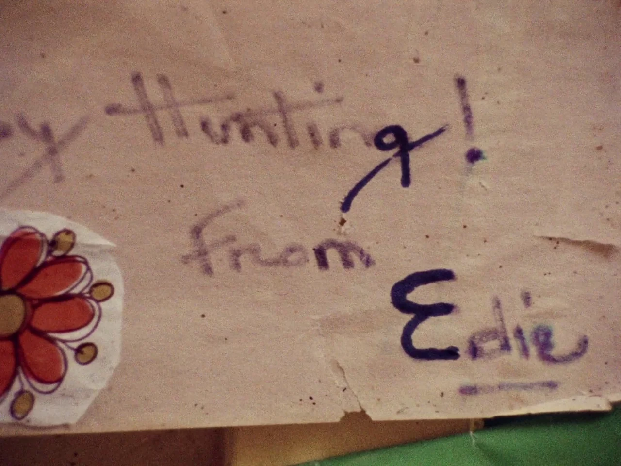 Grey Gardens (1975) movie still: closeup — A textured off-white piece of paper contains purple ink handwriting and a small sticker. The note reads…