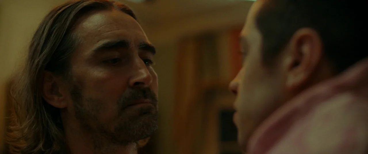 Bodies Bodies Bodies (2022) movie still: closeup — Two men are positioned closely together in a dim, shadowed indoor space. The man on the left…