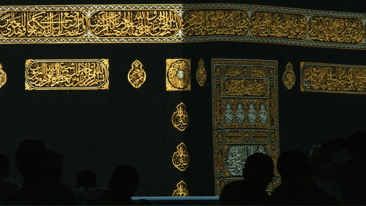 One Day in the Haram (2017) movie still: wide — The Kaaba stands as a massive black cube covered in intricate, embroidered gold Arabic calligraphy.…