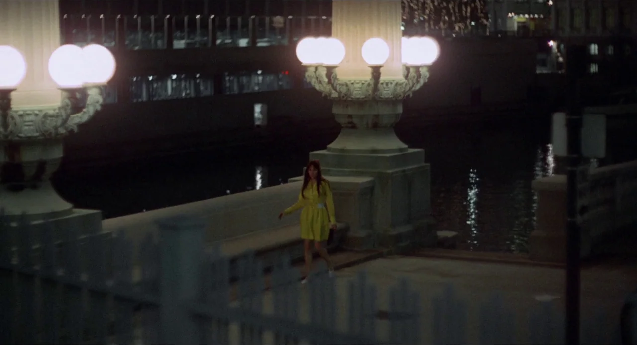 Medium Cool (1969) movie still: wide — A night view of a concrete riverwalk featuring prominent ornate white lampposts. A woman in a yellow dress…